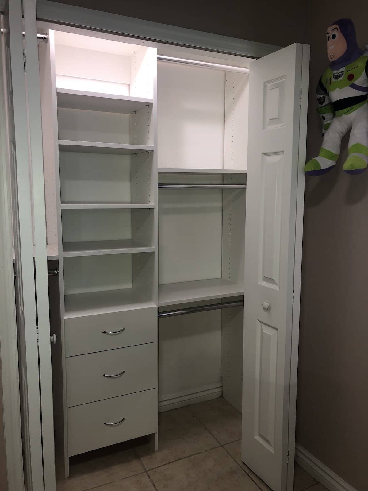 White reach-in closet with a shelf tower, three drawers and two levels of hanging rods, with a stuffed toy hanging on the open door