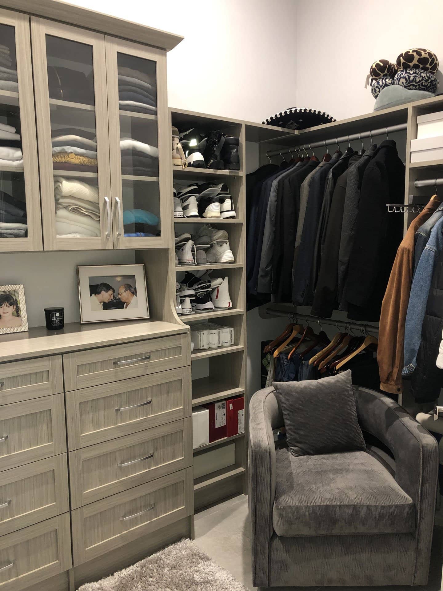 Walk-in closet with a glass-door hutch above a bank of drawers, open shoe shelves on both sides and a corner of hanging jackets