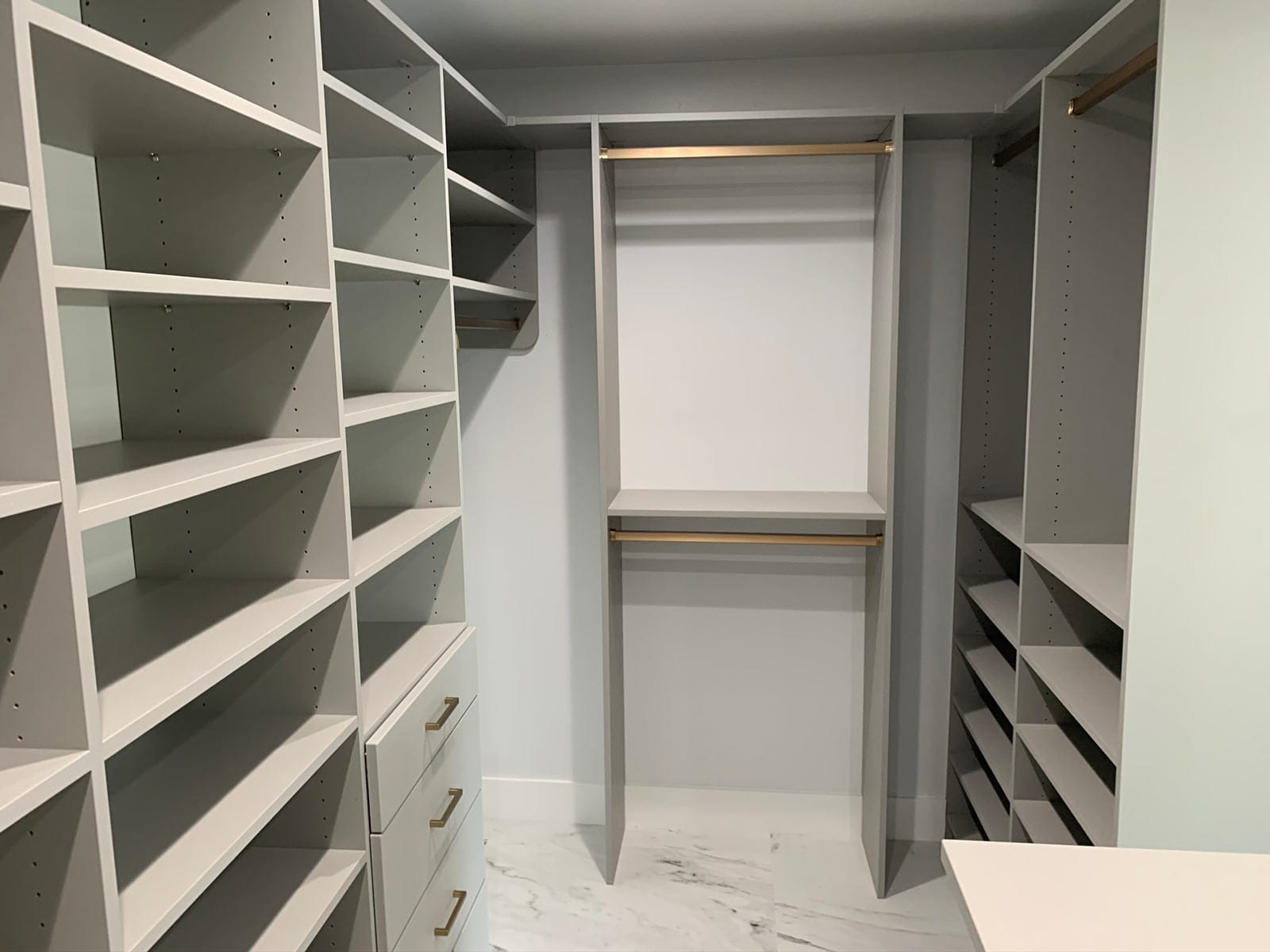 U-shaped walk-in closet in the Cloud finish with adjustable shelves on both sides, double-hang rods with gold-tone poles on the back wall and the corner of a small island