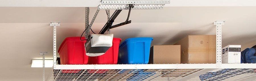 Overhead garage storage rack holding red and blue bins and boxes, mounted beside the garage door opener