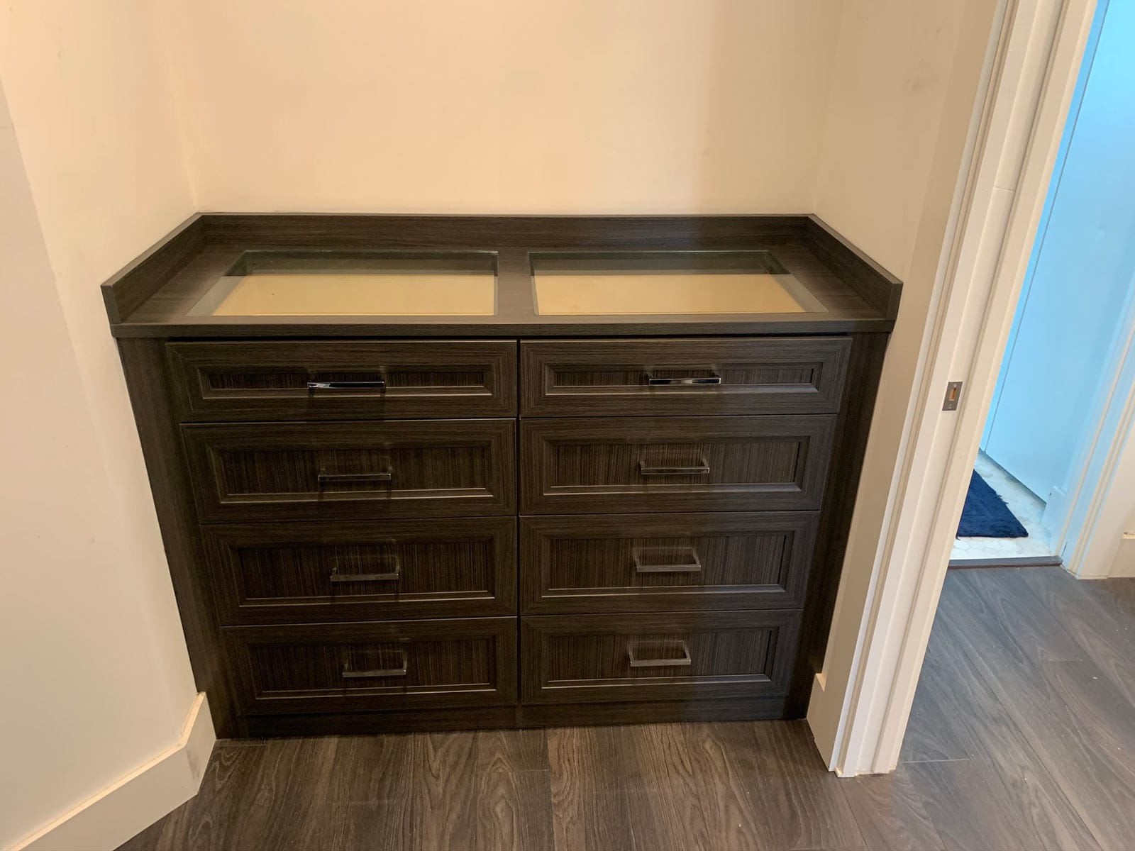 Built-in dresser in a dark Licorice wood-grain finish with raised-panel drawers, chrome pulls and a glass-topped display tray