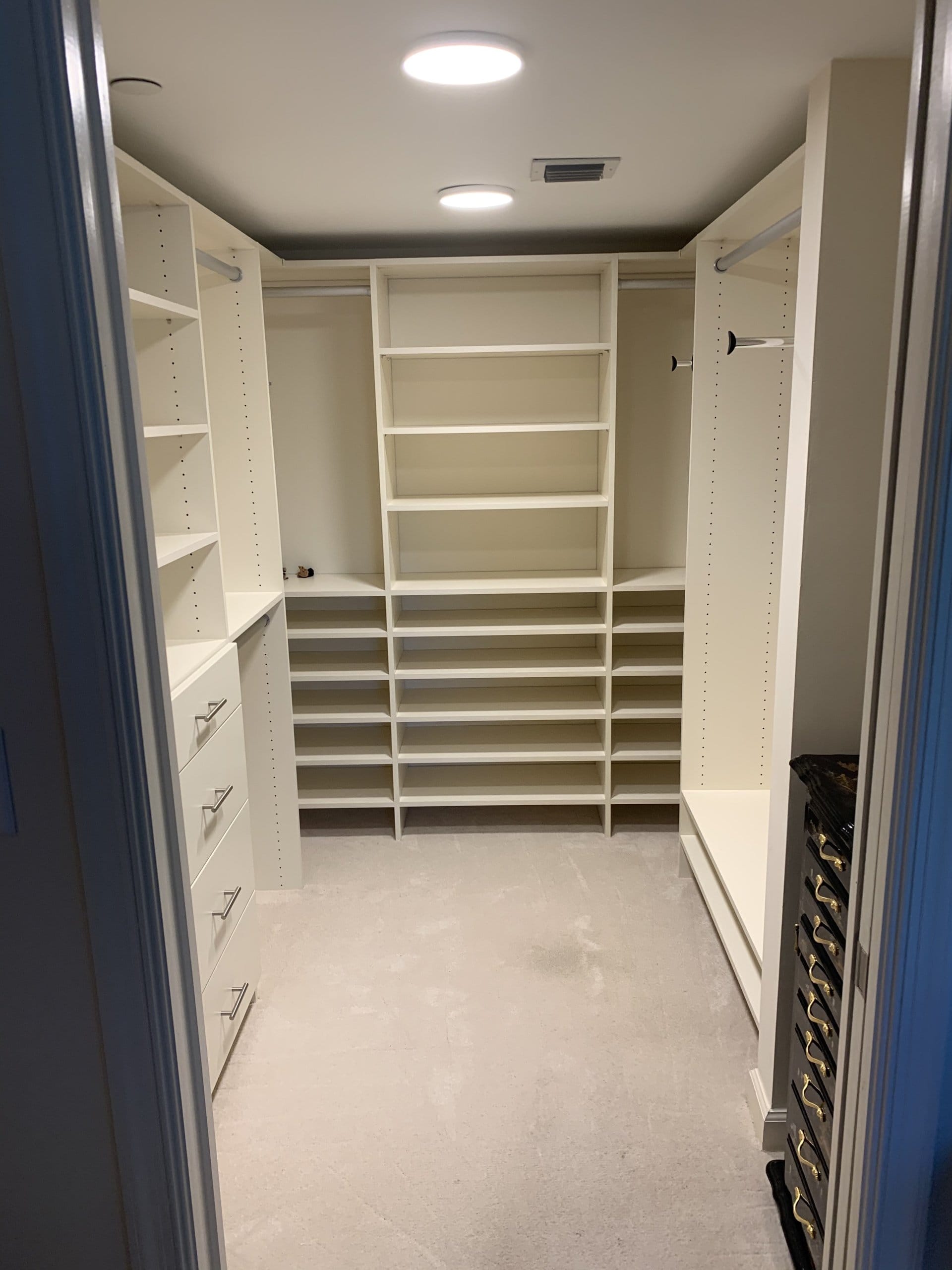 U-shaped walk-in closet with angled shoe shelves along the back wall, a drawer stack and adjustable shelving, photographed right after installation