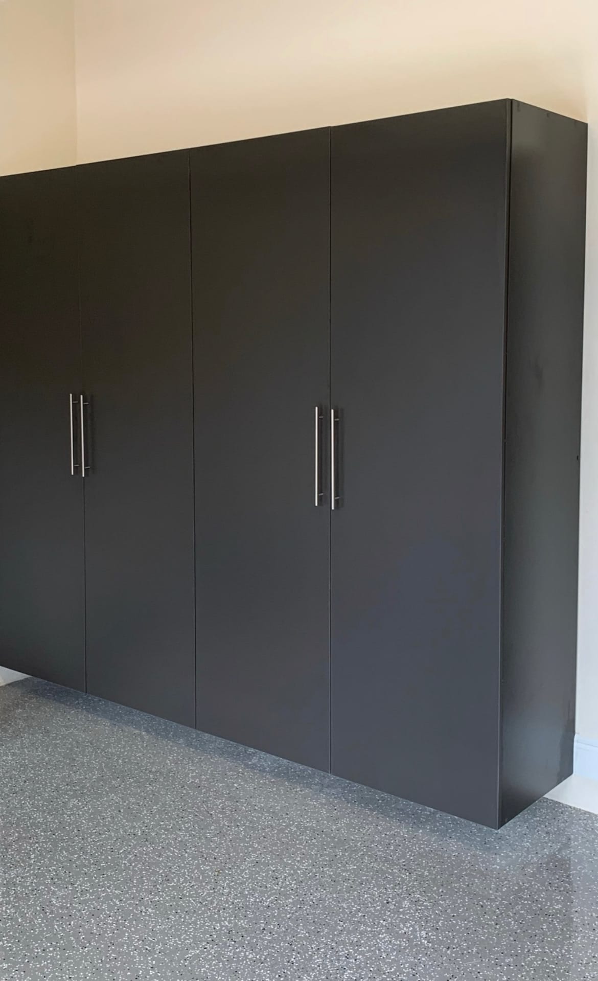 Tall black garage cabinets standing side by side along a garage wall above a speckled floor
