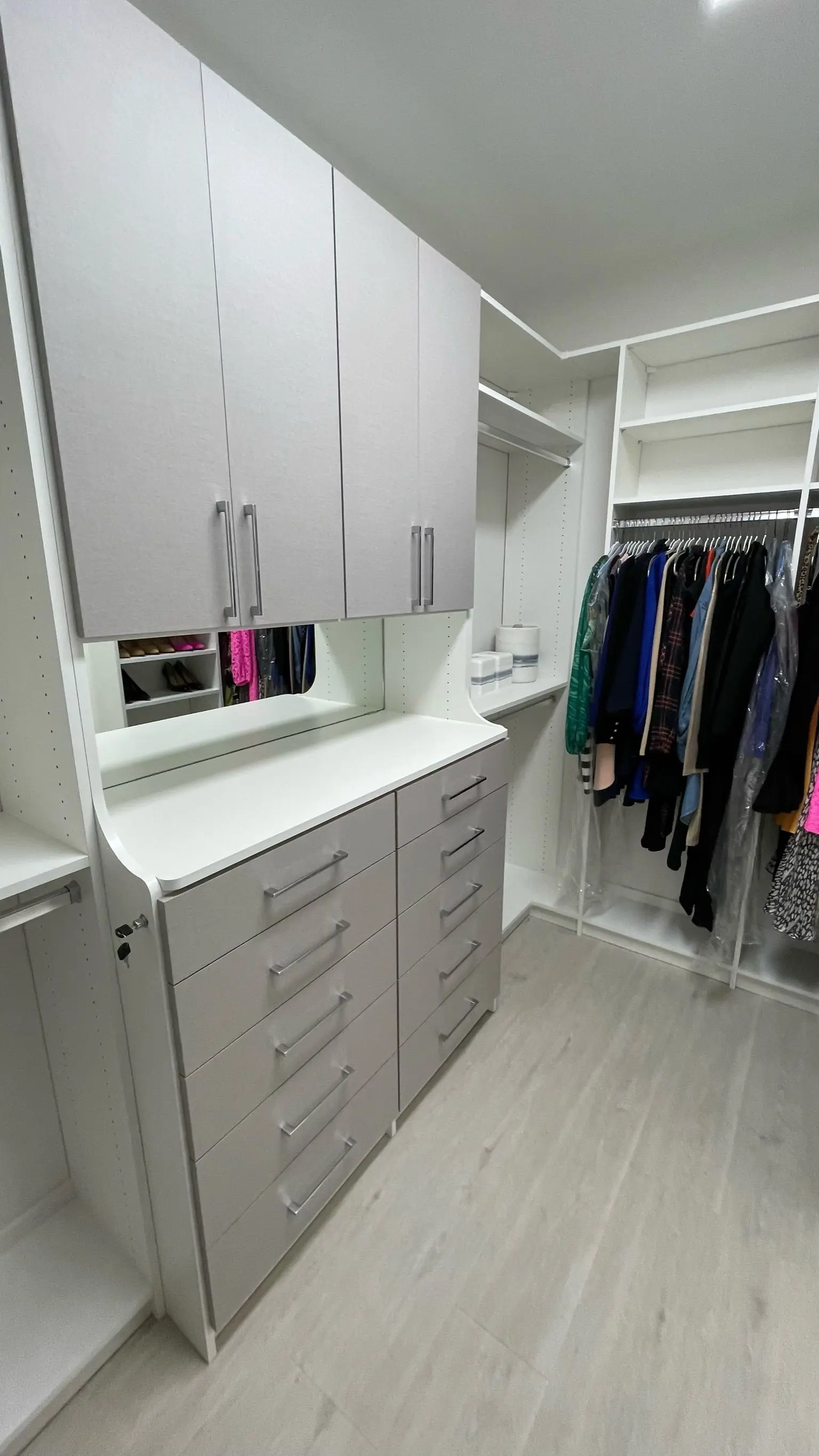 Custom walk-in closet with grey drawers, upper cabinets and hanging clothes